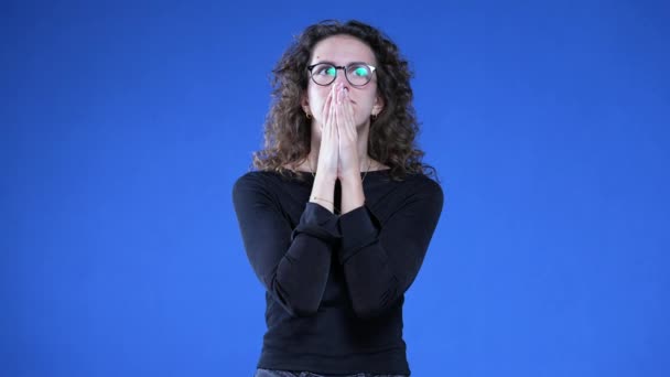 Κατειλημμένη Νεαρή Γυναίκα Στέκεται Μπλε Φόντο Κοιτάζοντας Ψηλά Χέρια Σφιγμένα — Αρχείο Βίντεο
