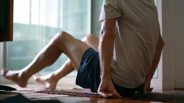 Senior man getting up from floor during morning exercise routine. elderly caucasian person sitting down in lotus position getting ready to meditate