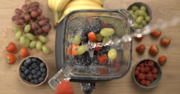 スローモーションでブレンダートップビューの視点に果物と水を注ぐ ベリーとブドウでスムージーを作る — ストック動画