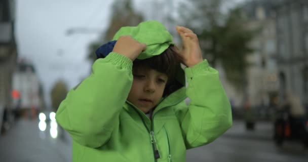 Yağmurdan Korunmak Için Kapüşonlu Yeşil Yağmurluk Giyen Çocuk Kaldırımda Dikiliyor — Stok video