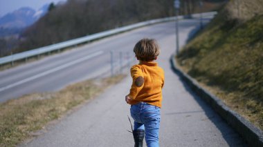 Arkadan, sarı kazaklı, kot pantolonlu ve botlu neşeli bir çocuk sonbahar manzarası boyunca koşuyor. Canlı koşu, gevrek sonbahar havasının heyecanını somutlaştırır.