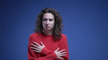 Korkmuş genç bir kadın korkusunu göstermekte tereddüt ediyor ve kırmızı süveter giyerek mavi arka planda panikliyor. 20 'li yaşlarda kadın.