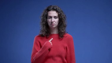 Suçlamalar karşısında şaşkına dönen, kendini inançsızlıkla işaret eden, mavi arka planda duran kadın. Komik bir şekilde 20 'li yaşlarda biri kendini gösteriyor.