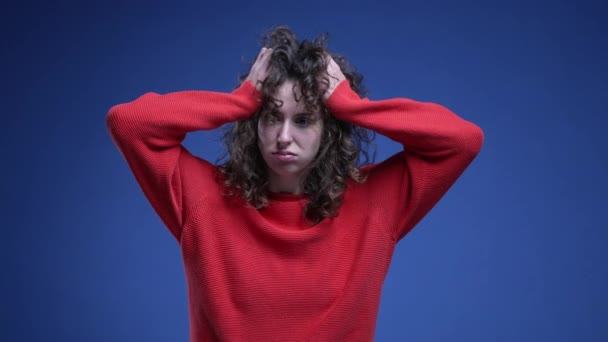 赤いセーターで青い背景に不安と絶望で彼女の髪を引っ張っている不思議な若い女性 気になる20代女性 — ストック動画