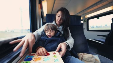Anne, oğlunu tren yolculuğunda evde okutuyor. Çocuk, okula gidip gelirken ebeveyniyle birlikte okul etkinliği yapıyor