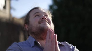 Sadık bir adam Tanrı 'ya dua ediyor gözlerini gökyüzüne açıyor ve gülümsüyor. Umut dolu erkek dışarıda namaz kılarken gülümsüyor.