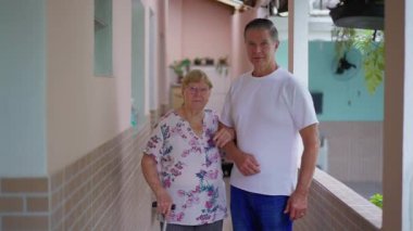 Yetişkin Oğul ve Yaşlı Anne arka bahçede kameraya poz veriyorlar. Orta yaşlı bir adam ve 80 'lerin yaşlı kadın portresi.