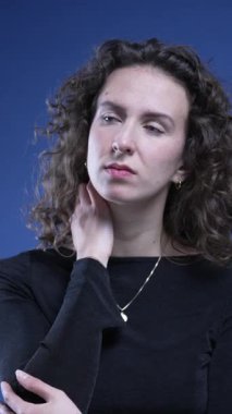 Stresli genç kadın boyun ağrısıyla boğuşuyor. Vücudunu ovuyor. Dikey videoda endişe duyuyor.