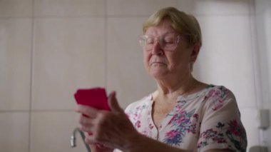 Evde Smartphone kullanan yaşlı kadın, Modern Teknoloji ile meşgul olan kıdemli bayanın Samimi Ev Hayatı