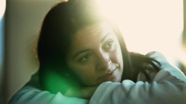 Thoughtful person thinking about life suffering from depression indoors with sunlight lens flare. Closeup pensive woman