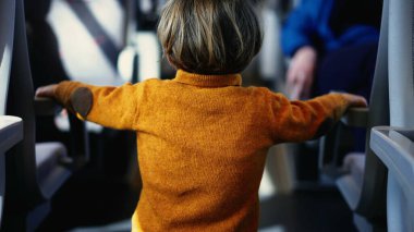 Güneşli sarı kazaklı bir çocuk tren koridorunda geziniyor, elleri koltuğun kolluklarını tutuyor. Küçük yolcu, demiryolu yolculuğu sırasında dikkat çekici bir kıyafetle zaman öldürüyor.