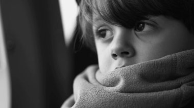 Eşarp takmış, siyah beyaz, düşünceli, derin zihinsel yansımasına bakan düşünceli bir çocuğun tek renkli yakın plan yüzü.