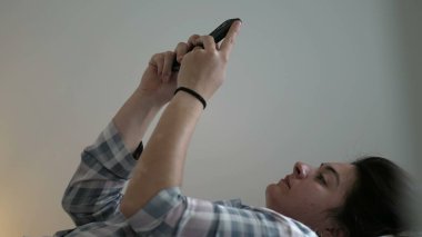 Yatakta pijamalarıyla telefona bakan dürüst bir kadın. Yatak odasında akıllı telefon cihazı kullanan sıradan bir aile içi olay yeri.
