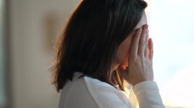 One worried woman standing by window with pensive preoccupied expression. Thoughtful anxious emotion of a female person thinking about problem