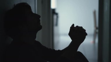 Person covering face in despair sitting on floor in the dark. Dramatic scene of depressed man