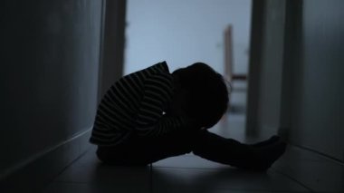 One scared desperate child covering face in fear sitting in dark corridor at home. Childhood loneliness and despair concept