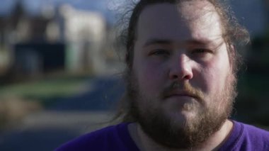 Ciddi bir ifadeyle kameraya bakan şişman bir gencin yakın çekim görüntüsü. Dışarıda duran bin yıllık bir erkeğin portresi.