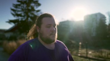 Düşünceli bir insan gün ışığında dışarıda yürüyor. Dalgın, kilolu bir gencin dış mekânda tefekkür ederken çekilmiş bir fotoğrafı.