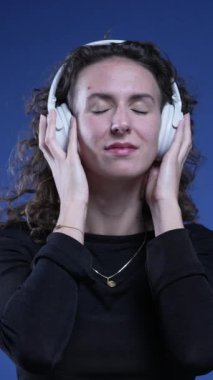 Müzik dinleyen kadın ellerini kulaklığın kenarına koyup şarkının tadını çıkarıyor, yakın plan insan yüzü, dikey video