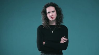 Kolları çaprazlanmış bir kadın donuk zeminde kameraya bakıyor.