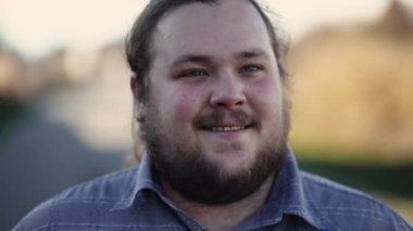 Kendinden emin, kilolu bir genç adam dışarı çıkıp gülümsüyor.