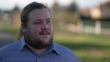 Açık havada kendine güvenen mutlu, kilolu bir genç adam. Caddedeki izleme çekiminde gülümseyen beyaz bir erkek portresi.