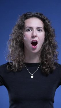 Kafası patlayan, elleri mavi arka planda duran bir kadın. Yakın çekim kişi dikey videoda aklını başından alıyor.