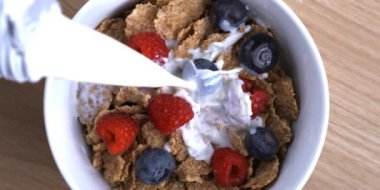 Üstünde ahududu ve yaban mersini olan buğday gevreğine süt dökmek, yukarıdan görülen yüksek hızlı kamerayla yakalanan süper yavaş çekim sabah kahvaltısı.