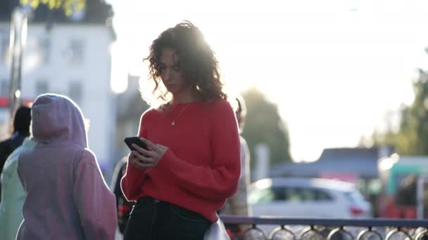 在城市日落时 与一群背景走路的人在电话中交谈 利用现代技术靠在金属栏杆上的人 — 图库视频影像