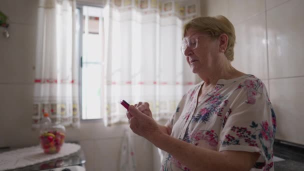 キッチンで携帯電話を使用する高齢女性 技術を使用してシニアの国内ライフスタイルシーン — ストック動画