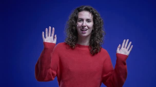 Cheerful Woman Red Sweater Greeting Hand Wave Blue Background — Stock Video