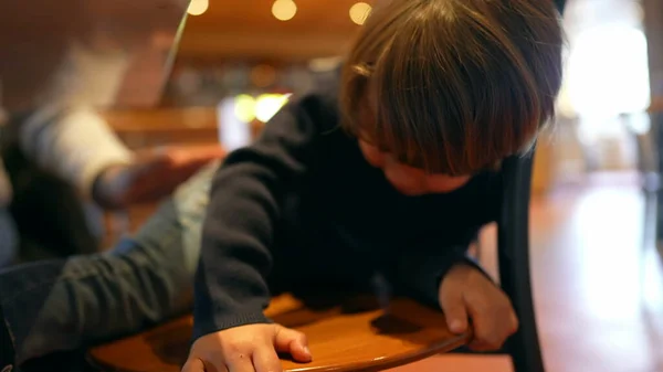 Small boy trying to climb on top of chair at restaurant, little male caucasian kid sitting