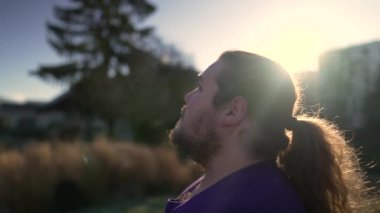 Dalgın, kilolu bir genç adam açık havada durup gökyüzüne bakıyor. Umut ve FAITH ile. Mutlu insan yüzünü kapat.