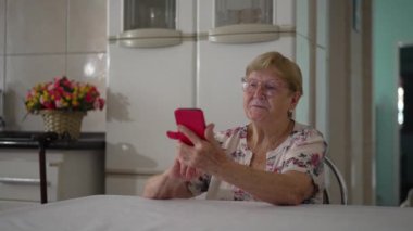 Ev mutfağında cep telefonu kullanan kıdemli bir kadın. 80 'li yıllarda, modern teknolojiyle etkileşimde olan, samimi, otantik, yaşlı bir insan.