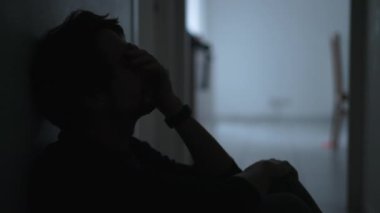 Depresyonda olan bir genç adam zihinsel hastalıktan muzdarip olarak yerde oturuyor ve yüzünü pişmanlıkla örtüyor. Erkek kişi endişeli ve depresyonda.