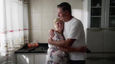 Yetişkin oğul, mutfakta duran yaşlı anneyi kucaklıyor. Otantik gerçek insan yaşam tarzı. Erkek kıdemli kadınla etkileşime girer, aile değerleri yaşlılarla ilgilenir.