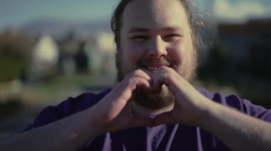 Mutlu adam dışarıda, gün ışığında kalp sembolü çiziyor. Şefkatli insan sevgisini gösterir