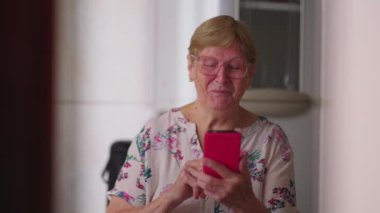 Akıllı telefon cihazıyla kameraya gülümseyen mutlu son sınıf kadını. Modern teknolojiyle ev içi yaşam tarzı, 80 'li yaşlarda yaşlı bir kadın.