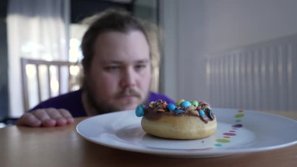 ドーナツの前に座っている1人の太りすぎの若者は砂糖の甘い不健康なスナックを食べることを控えています — ストック動画