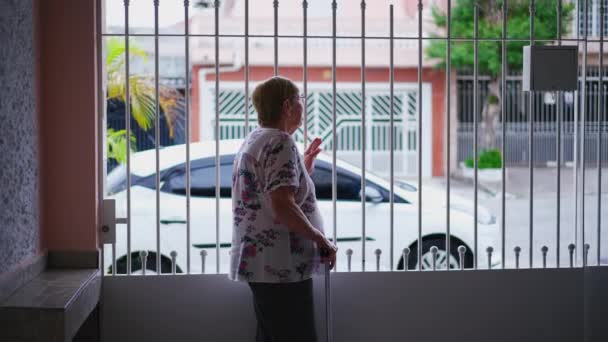 Наблюдая Дома Пожилой Женщины Стоящей Внутри Дома Видом Тротуар Держа — стоковое видео