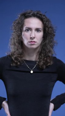 Kadın, ShoCK ve inançsızlığa eliyle ağzını kapatarak ve mavi arka planda dikey video kameraya bakarak tepki veriyor.