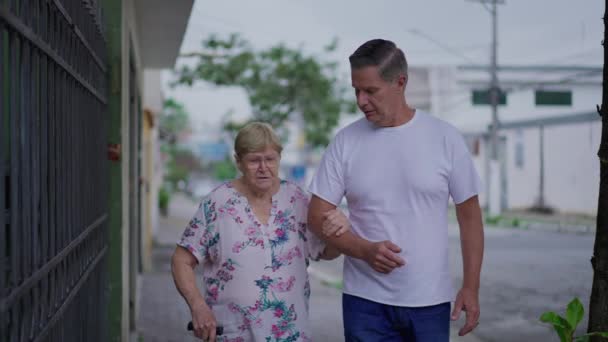 Yetişkin Oğul Yaşlı Annenin Kaldırımda Yürümesine Yardım Ediyor Bir Erkek — Stok video
