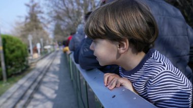 Vagondan eğilen, İsviçre Vapeur 'unda minyatür tren sürerken demiryolu manzarasını izleyen mutlu küçük çocuk.