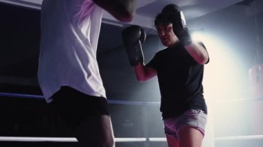 Muay Thai rakipleri Dramatik Aydınlık Boks ringinde Tekme ve Yumruk Karşılaşması. Rakip dirsek dövüşçüsü eldiven giyiyor.