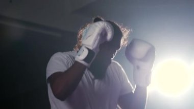 İki boks ringinin içinde karşı karşıya gelen iki dövüşçü arka plandaki ışıkla çarpışıyor, Muay Thai antrenman maçı iki adam arasında.