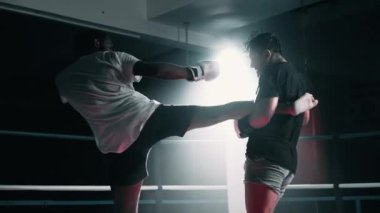 Muay Thai dövüşçüleri boks ringinde tekmeleşiyorlar. Işıklar parlıyor genç adamlar kavga ediyor