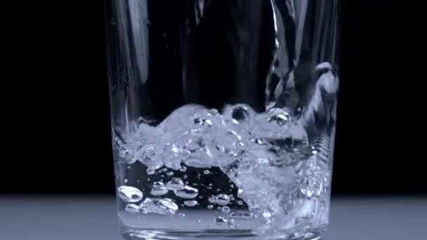 ブラックバックドロップのスーパースローモーションでガラスカップに水を注ぐ 液体スプラッシュを提供する — ストック動画