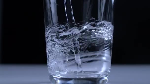 ブラックバックドロップで高速カメラでキャプチャされた超スローモーションでガラスカップに水を注ぐ — ストック動画