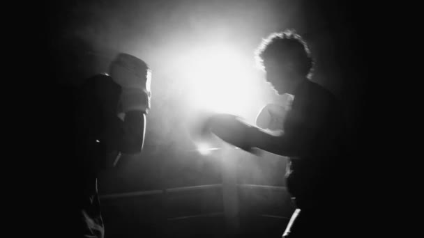 ボクシングリング内部の戦闘機は 劇的なモノクロ 黒と白のバックライトで敵を打つ ライバルを打つ手袋を着ている若い男性 — ストック動画