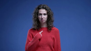 Suçlamalar karşısında şaşkına dönen, kendini inançsızlıkla işaret eden, mavi arka planda duran kadın. Komik bir şekilde 20 'li yaşlarda biri kendini gösteriyor.